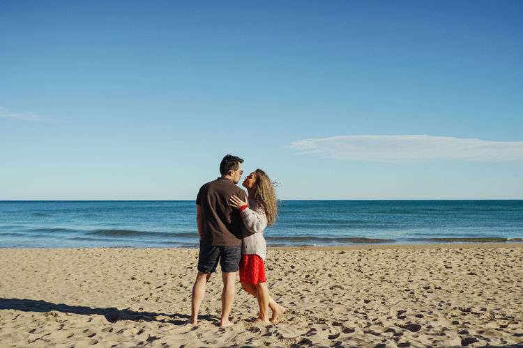 Rear view of woman with man standing at beach against clear sky