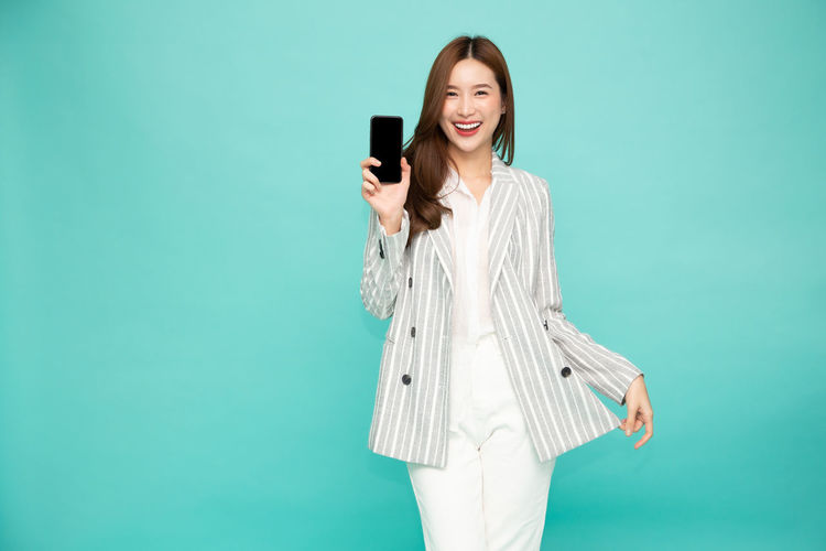 Smiling young woman using smart phone while standing against blue sky