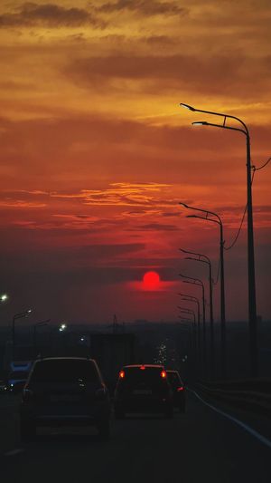 Cars on street against dramatic sky during sunset