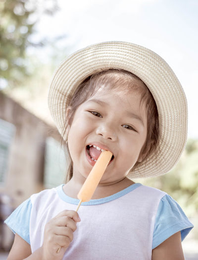 Close-up portrait of cheerful girl eating popsicle outdoors