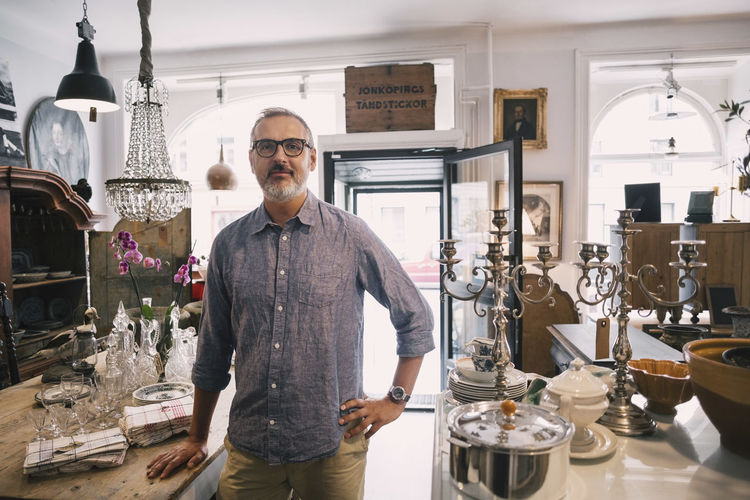 Portrait of confident owner standing with hand on hip in antique store
