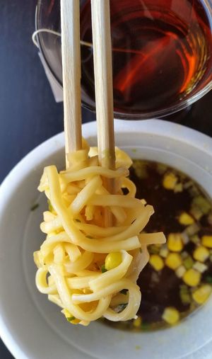 Close-up of noodles on chopsticks against green tea and bowl