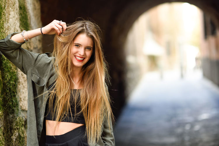 Portrait of smiling young woman with hand in hair standing on street