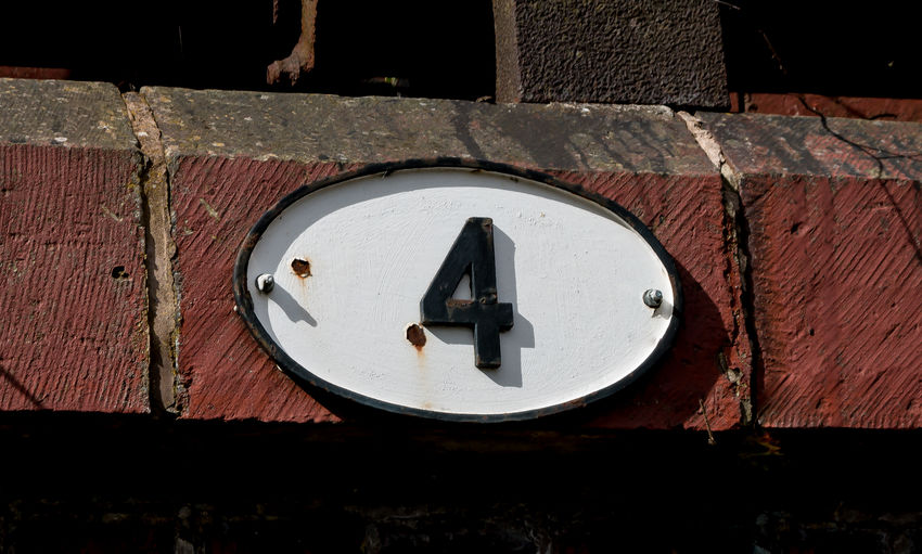A black number four on an oval white plate fixed to a stone and brick wall