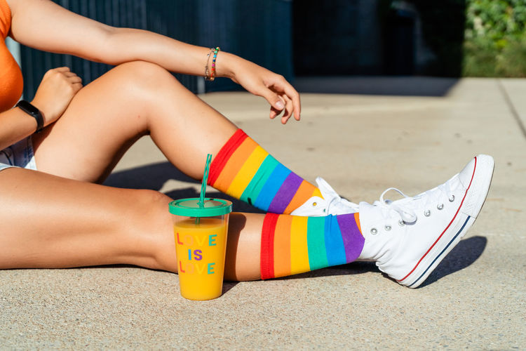 Girl wearing bright colorful rainbow pride socks sitting on ground outdoors.  lifestyle, pride month 