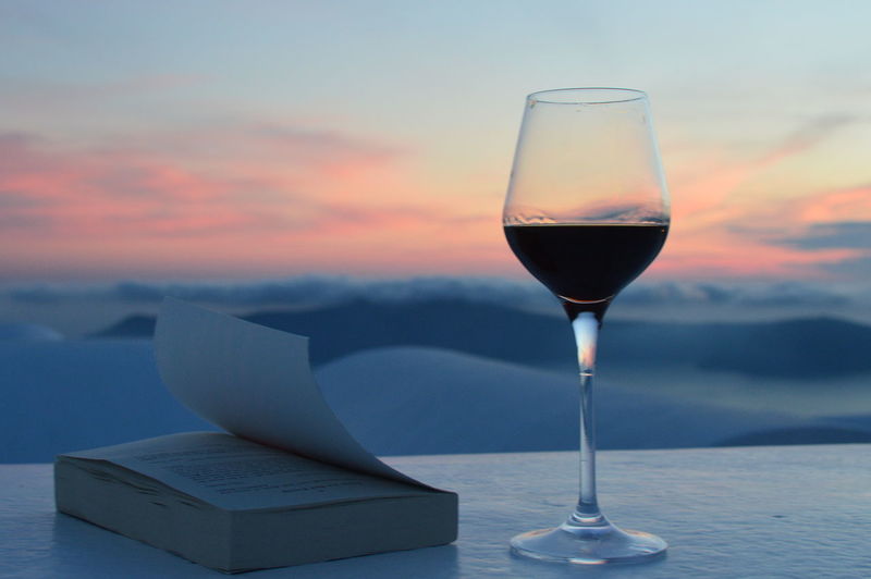 Wineglass with book on table against sky during sunset