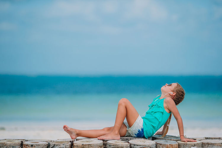 Full length of girl sitting at beach against sky