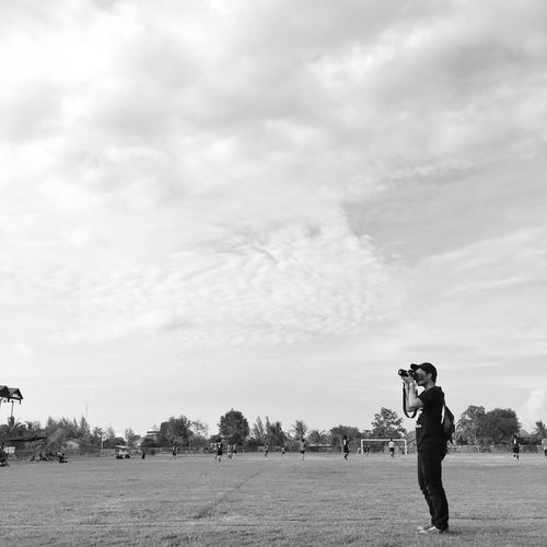 Man photographing while standing on field against cloudy sky