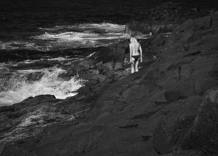 Rear view of shirtless woman standing on rock by sea
