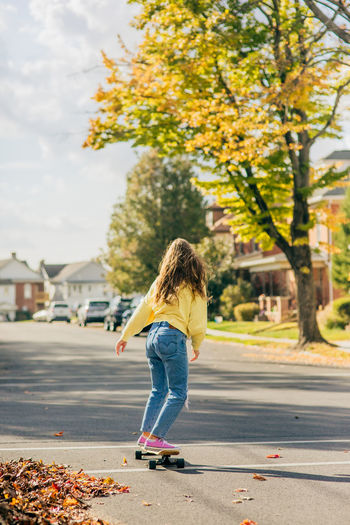 Girl long boarding down the street with the sun in her flowing hair during the autum season