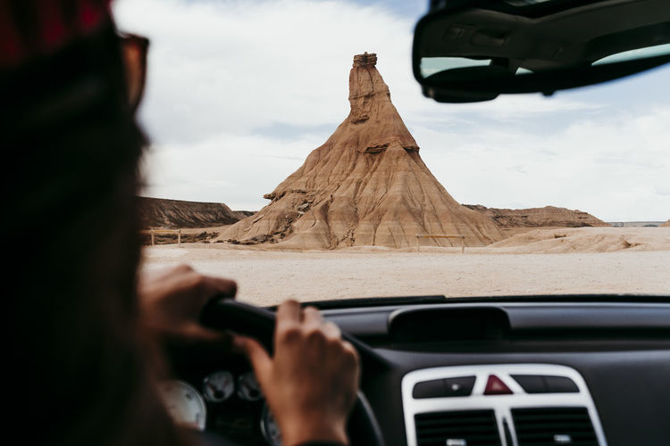 Spain, navarre, young woman driving car toward sandstone rock formation in bardenas reales