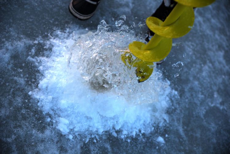 Low section of person drilling ice for fishing