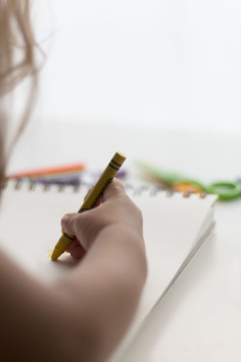 Cropped image of child painting on book with crayon
