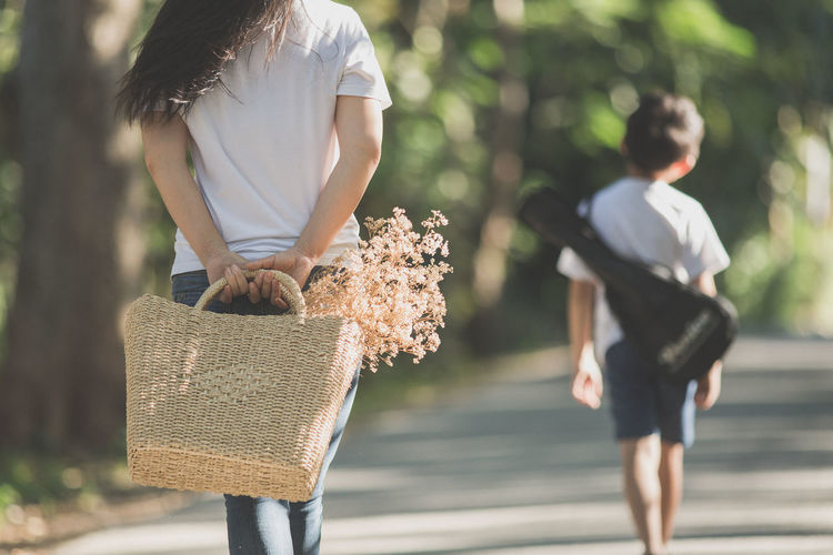 Midsection of woman carrying plants on wicker bag with boy walking on road in background