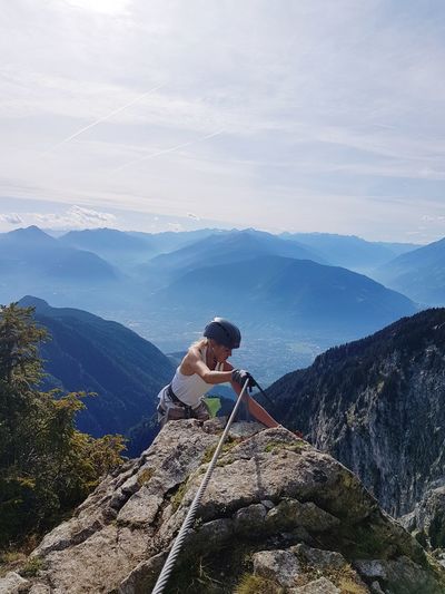 Woman climbing on rock by mountains against sky