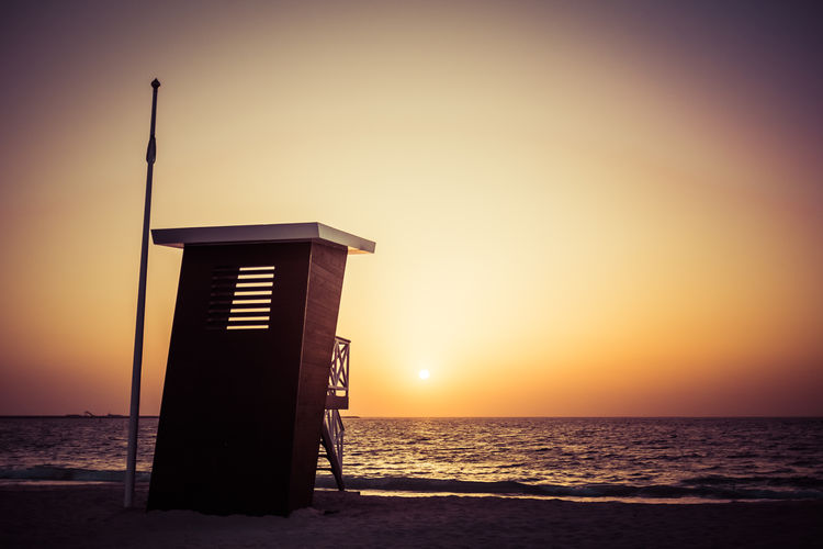 Lifeguard hut at beach against clear sky during sunset
