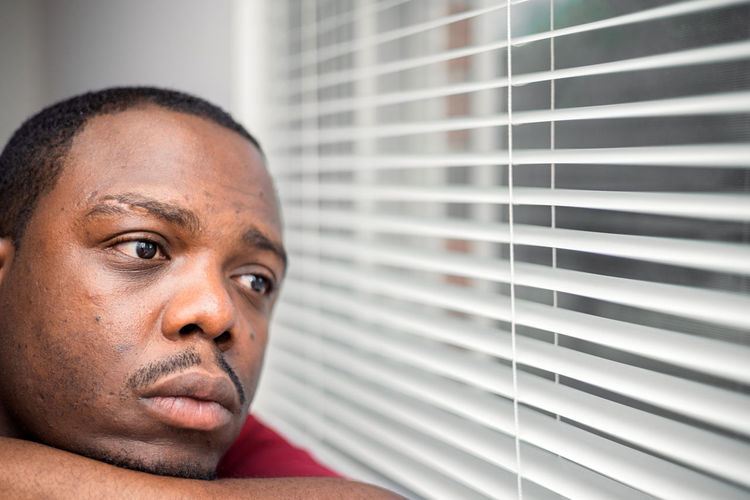 Young depressed or anxious african american man in bedroom at home sitting