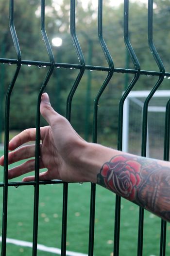 Cropped hand of man with tattoos holding wet fence during rainy season
