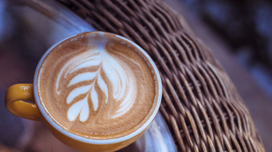 Hot latte on woven table.close up coffee art leaf design .art of latte espresso
