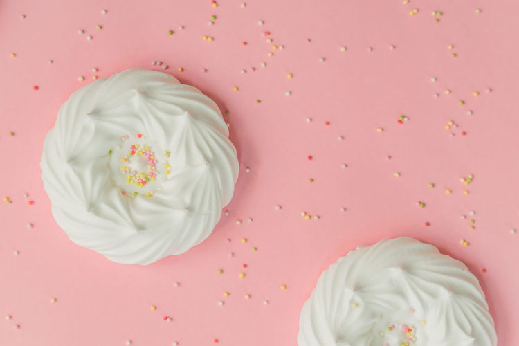 Homemade white air meringues and confectionery decorations on pink background