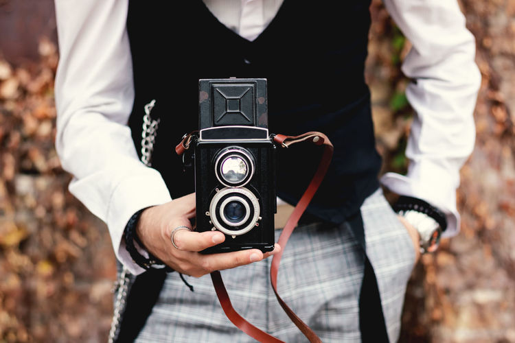 Close-up of man photographing with vintage medium format photo camera outdoors.