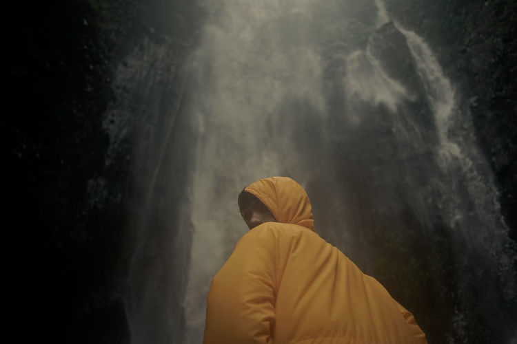 Rear view of man standing against yellow waterfall