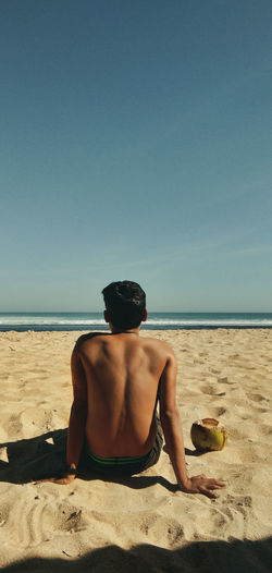 Rear view of shirtless man sitting on beach
