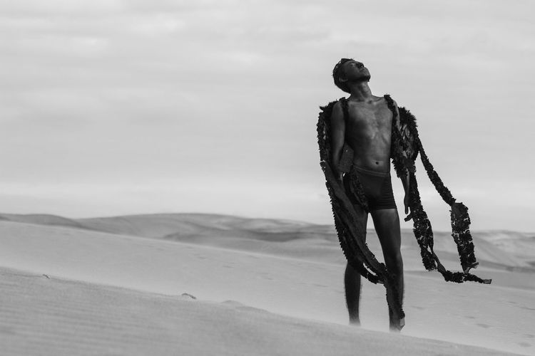 Teenage boy in costume on desert against sky