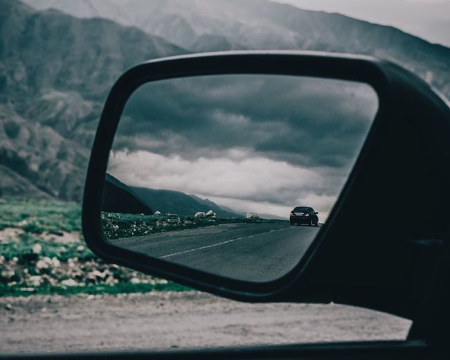 Reflection of car against storm clouds on side-view mirror