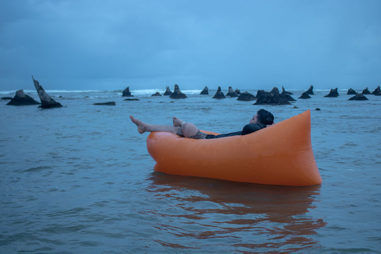 Full length of man relaxing on inflatable pool raft in sea