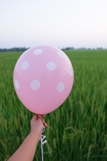 Cropped hand holding helium balloon by farm