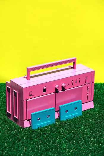 Bright pink vintage cassette player with two blue cassettes placed on green grass against yellow background in studio