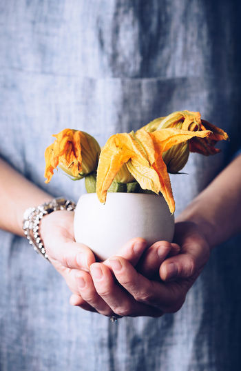 Midsection of woman with flowers in bowl standing indoors
