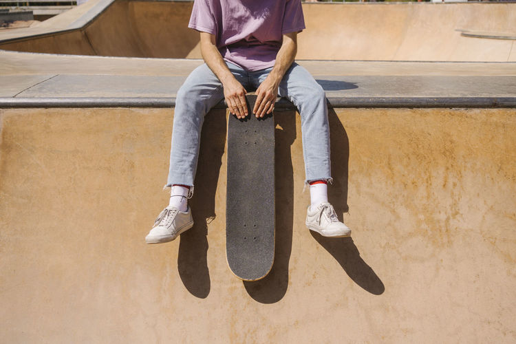 Man holding skateboard sitting at sport ramp on sunny day