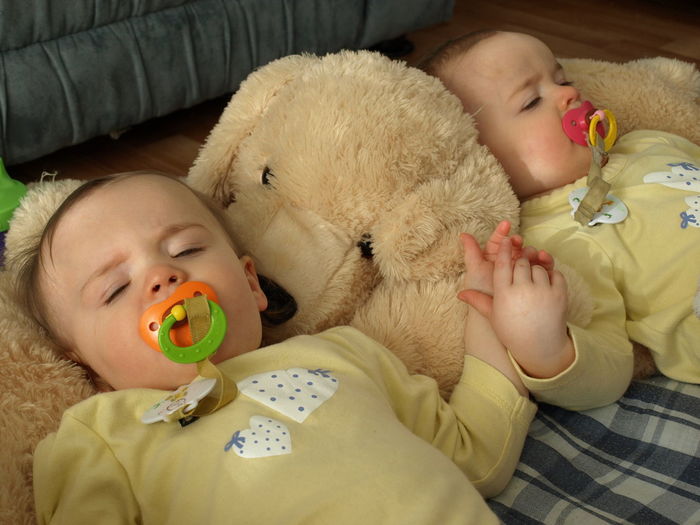 Portrait of twin girls lying down on bed at home with giant bear