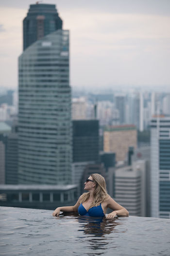 Woman relaxing in swimming pool against cityscape