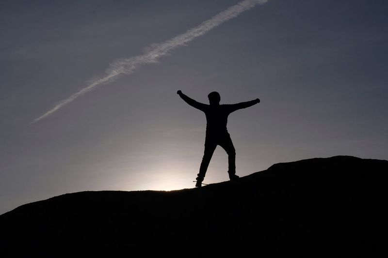 Silhouette man with arms outstretched standing on mountain against sky