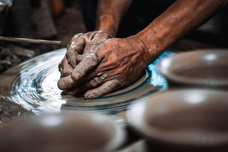 Cropped hands of person working with mud on pottery wheel