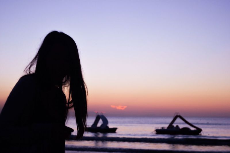 Silhouette woman sitting on beach against clear sky during sunset