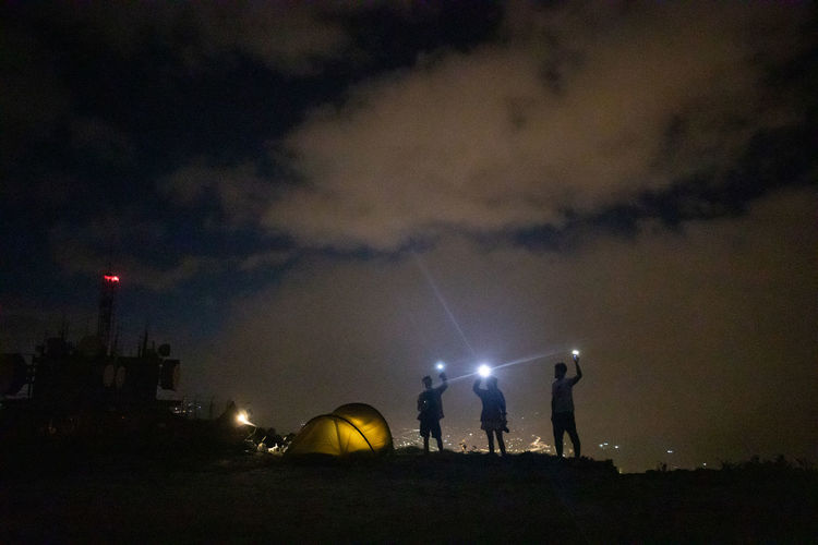 Silhouette people on illuminated field against sky at night