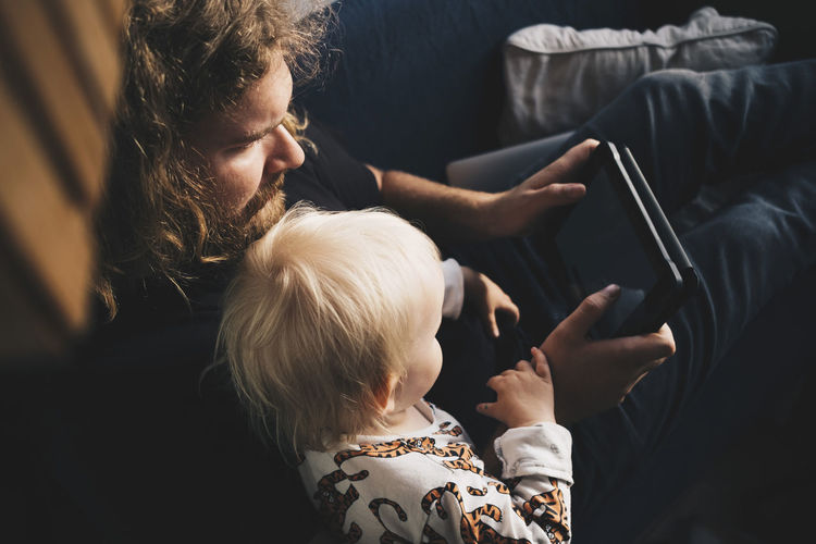 Father showing digital tablet to girl while sitting on sofa at home