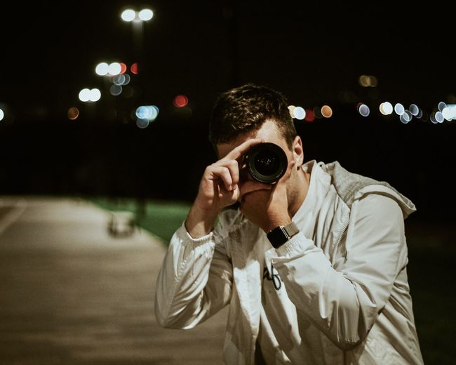 Portrait of young man holding camera at night