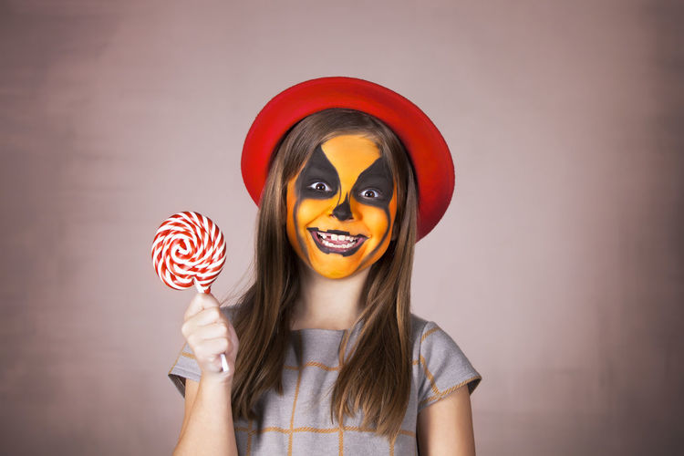 Smiling girl with painted face holding lollipop