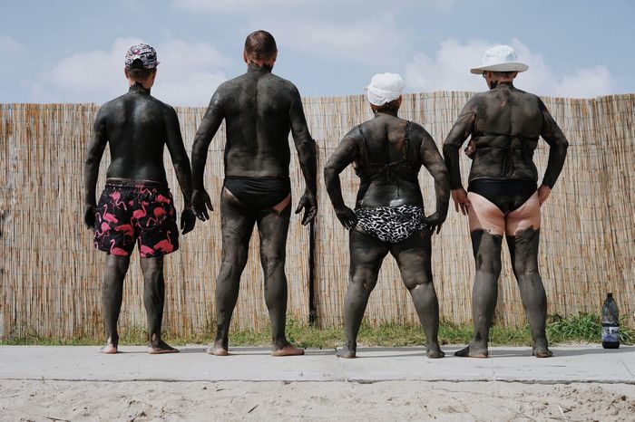 Rear view of friends covered in mud at beach