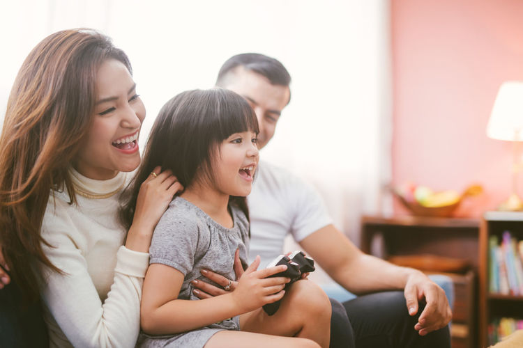 Happy parents with daughter holding joystick while sitting at home