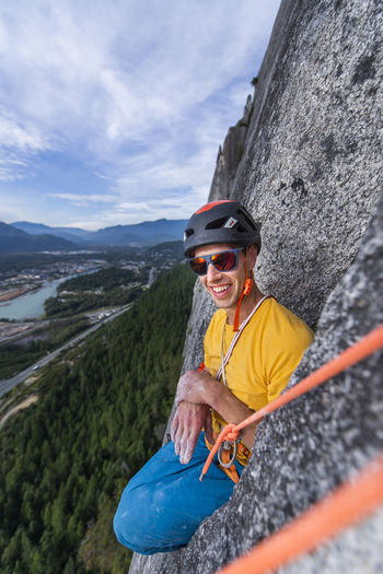 Man sitting funny position while rock climbing with helmet sunglasses