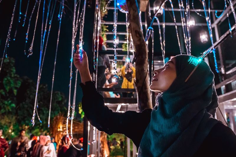 Young woman wearing hijab holding decoration at night