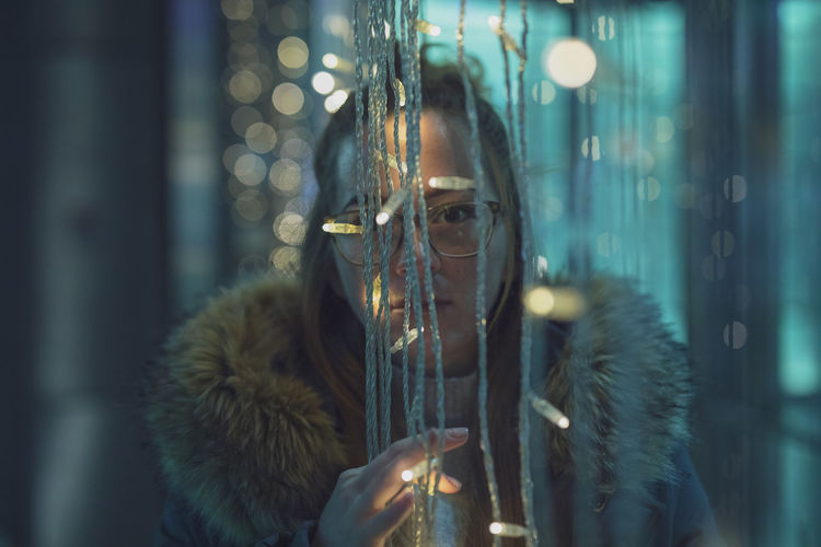 Portrait of young woman by illuminated string lights 
