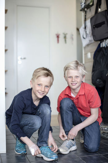 Portrait of smiling boys tying shoe laces on floor