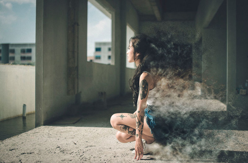 Digitally generated image of woman wearing shorts with tattoo crouching in abandoned building